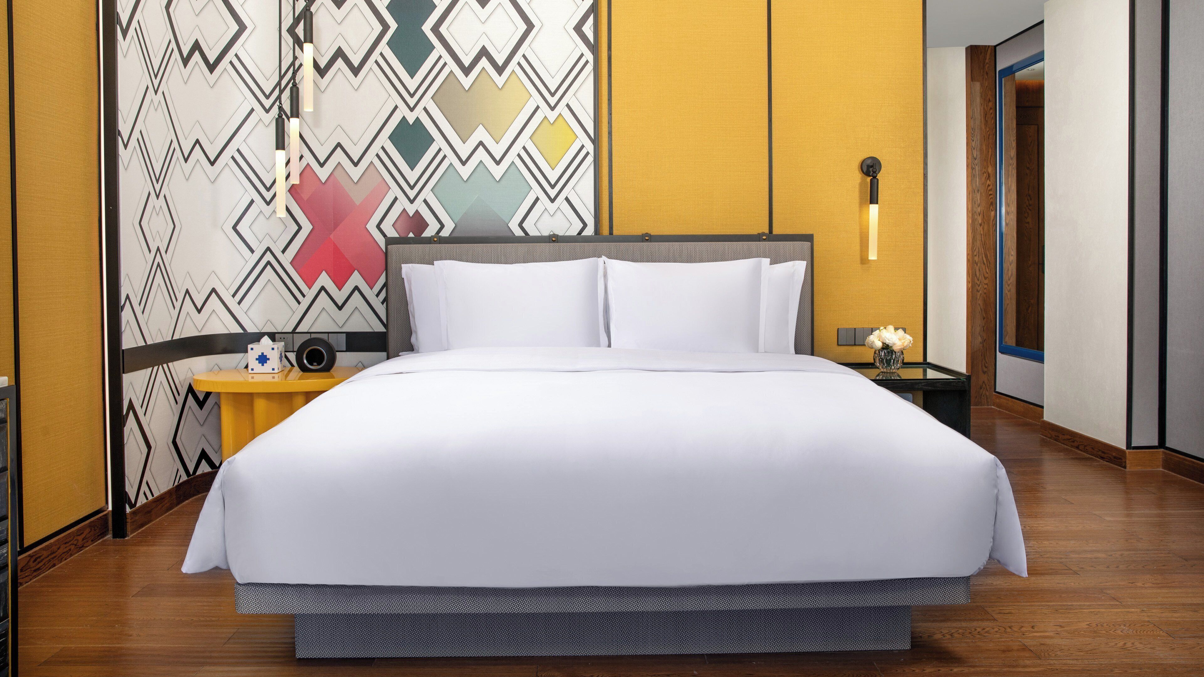Una habitación de hotel con una cama grande, una mesita de noche con lámpara y un papel tapiz estampado.
