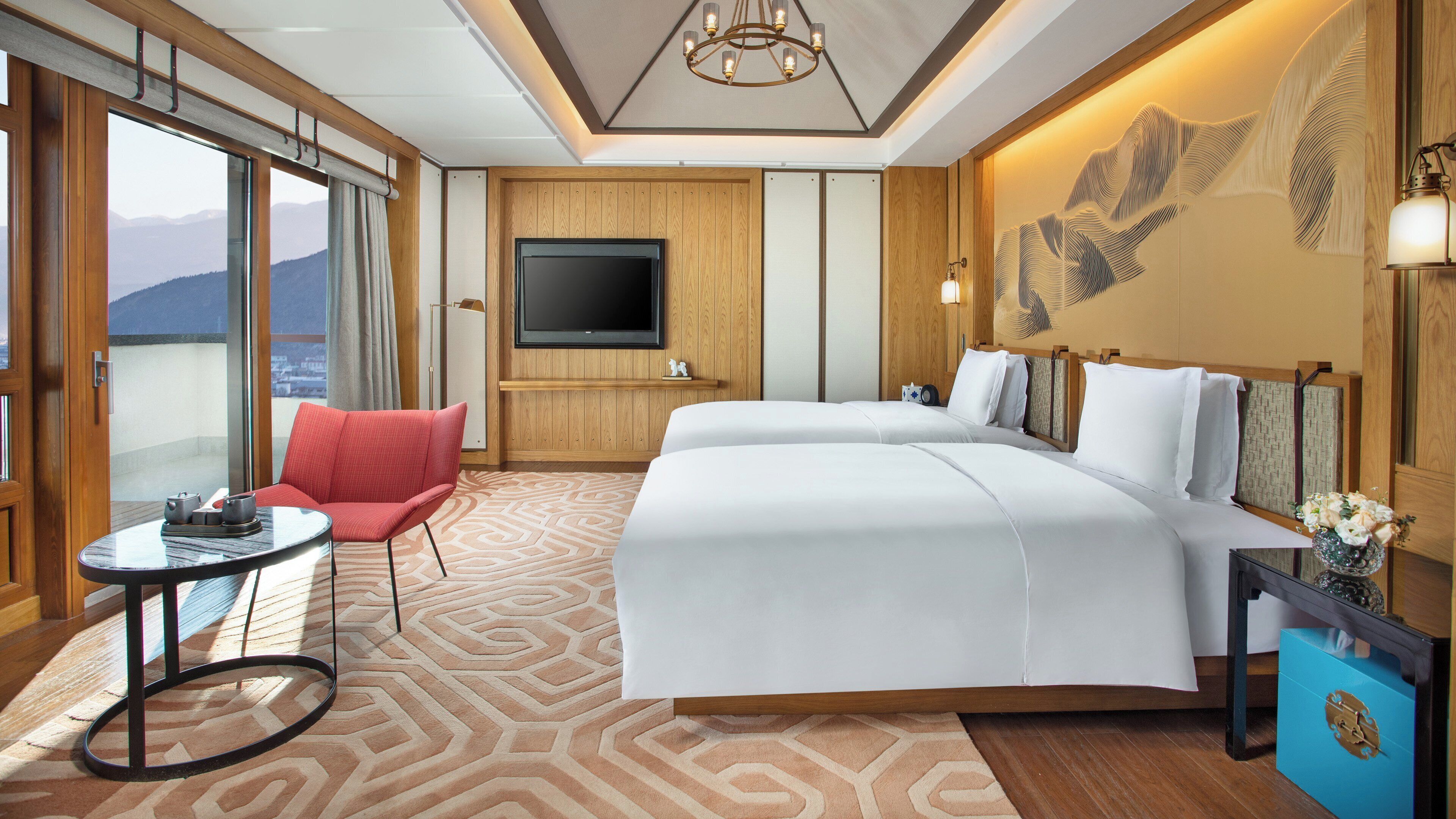Ein Hotelzimmer mit einem großen Bett, einem roten Sessel, einem Fernseher und Blick auf Berge.