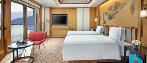 Ein Hotelzimmer mit einem großen Bett, einem roten Sessel, einem Fernseher und Blick auf Berge.
