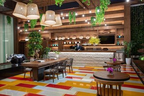Zona de bar moderna con detalles de madera, plantas colgantes y un colorido diseño en el suelo.
