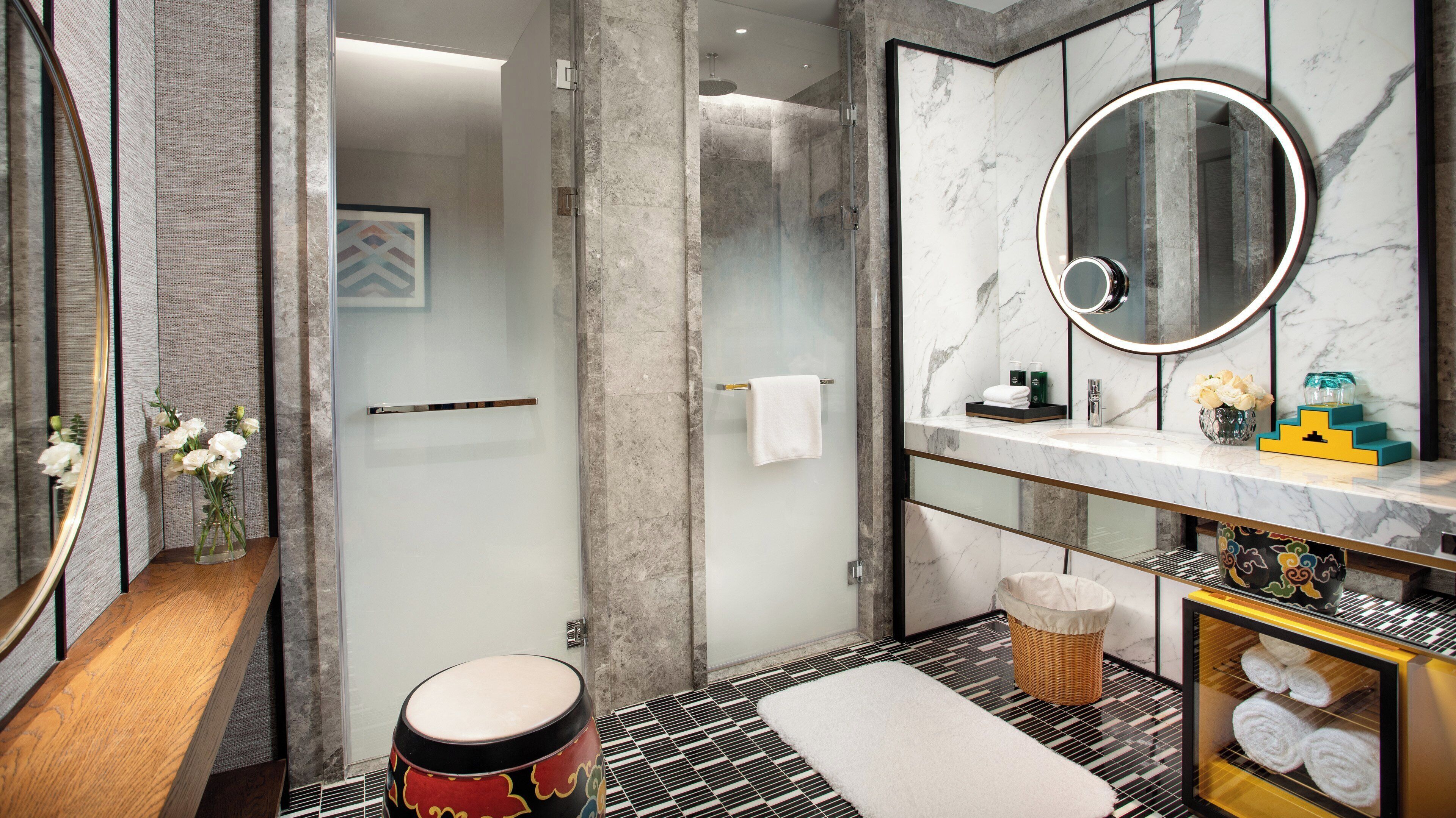 Une salle de bain moderne avec une douche à parois de verre, un meuble-lavabo en marbre et un miroir rond.