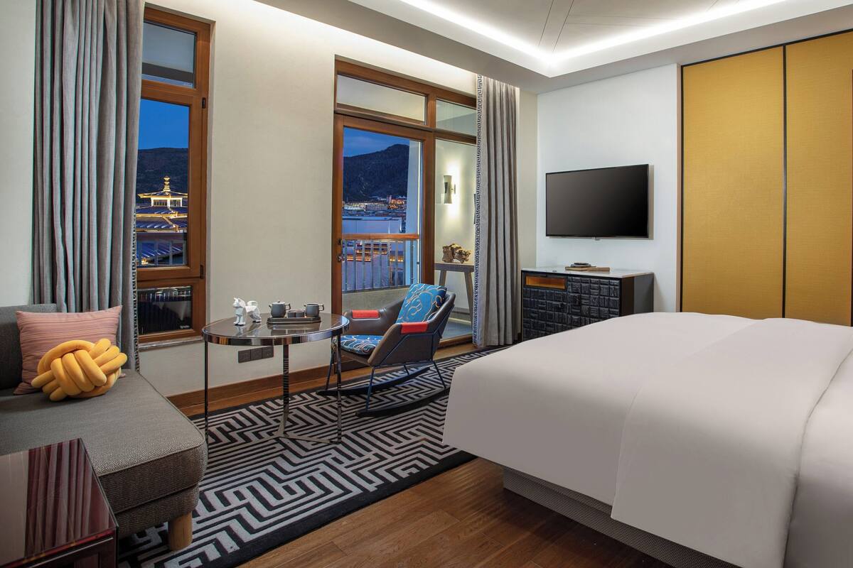 Une chambre d’hôtel avec un grand lit, une télévision, un bureau avec une chaise et une vue sur le paysage urbain par la fenêtre.