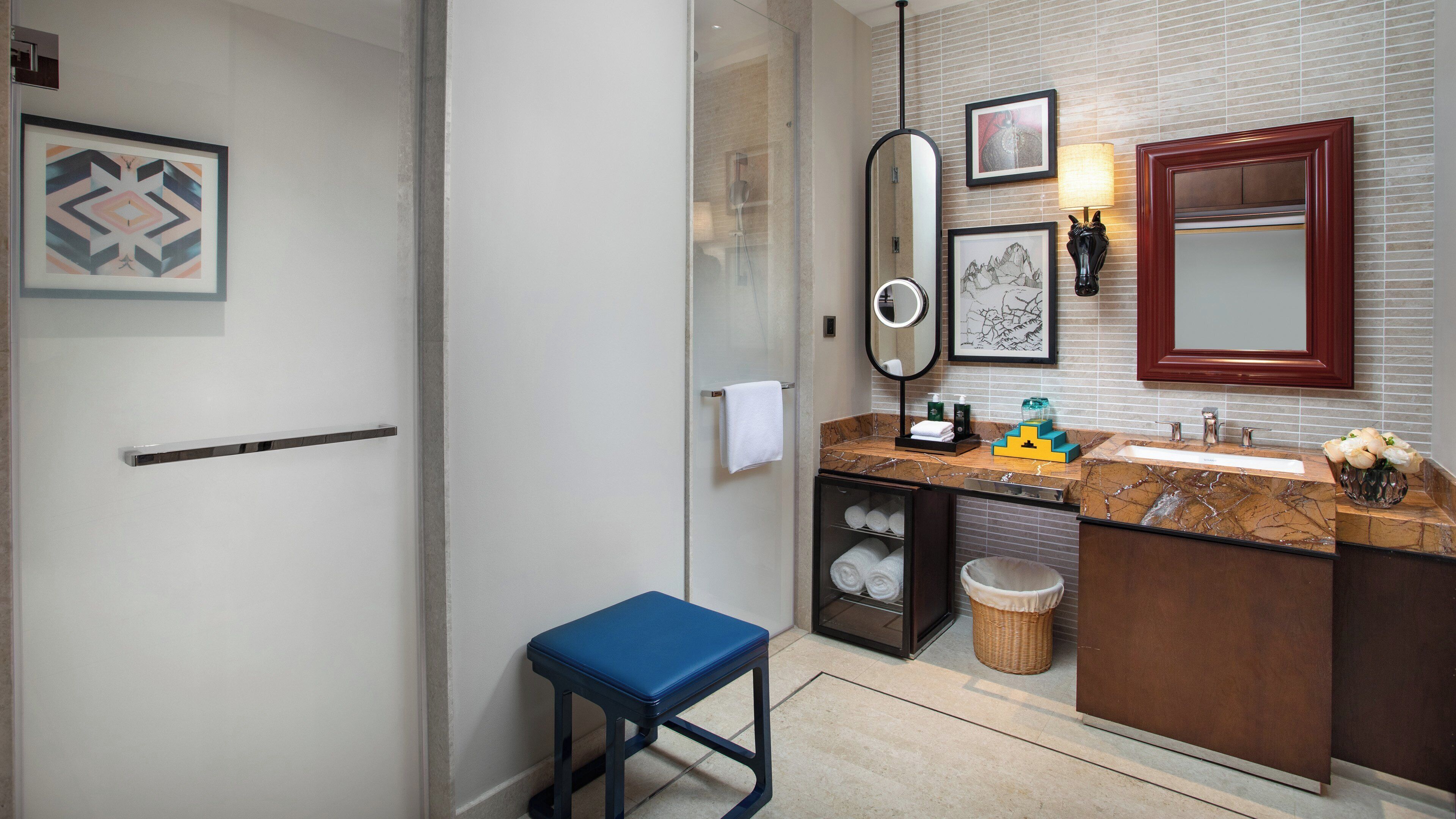 A modern bathroom with a glass shower enclosure, a marble sink, and a blue stool.