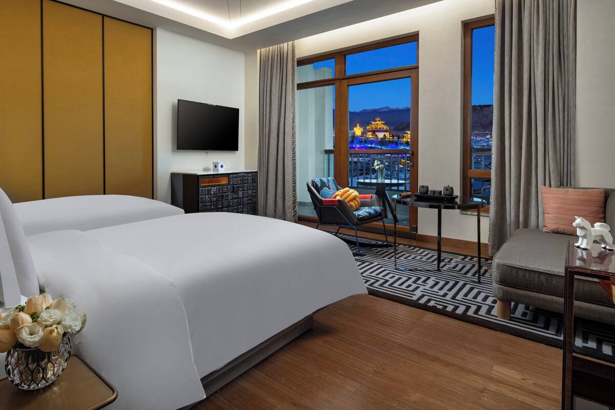 Une chambre d’hôtel avec un grand lit, une télévision, un bureau avec une chaise et une vue sur un immeuble par la fenêtre.