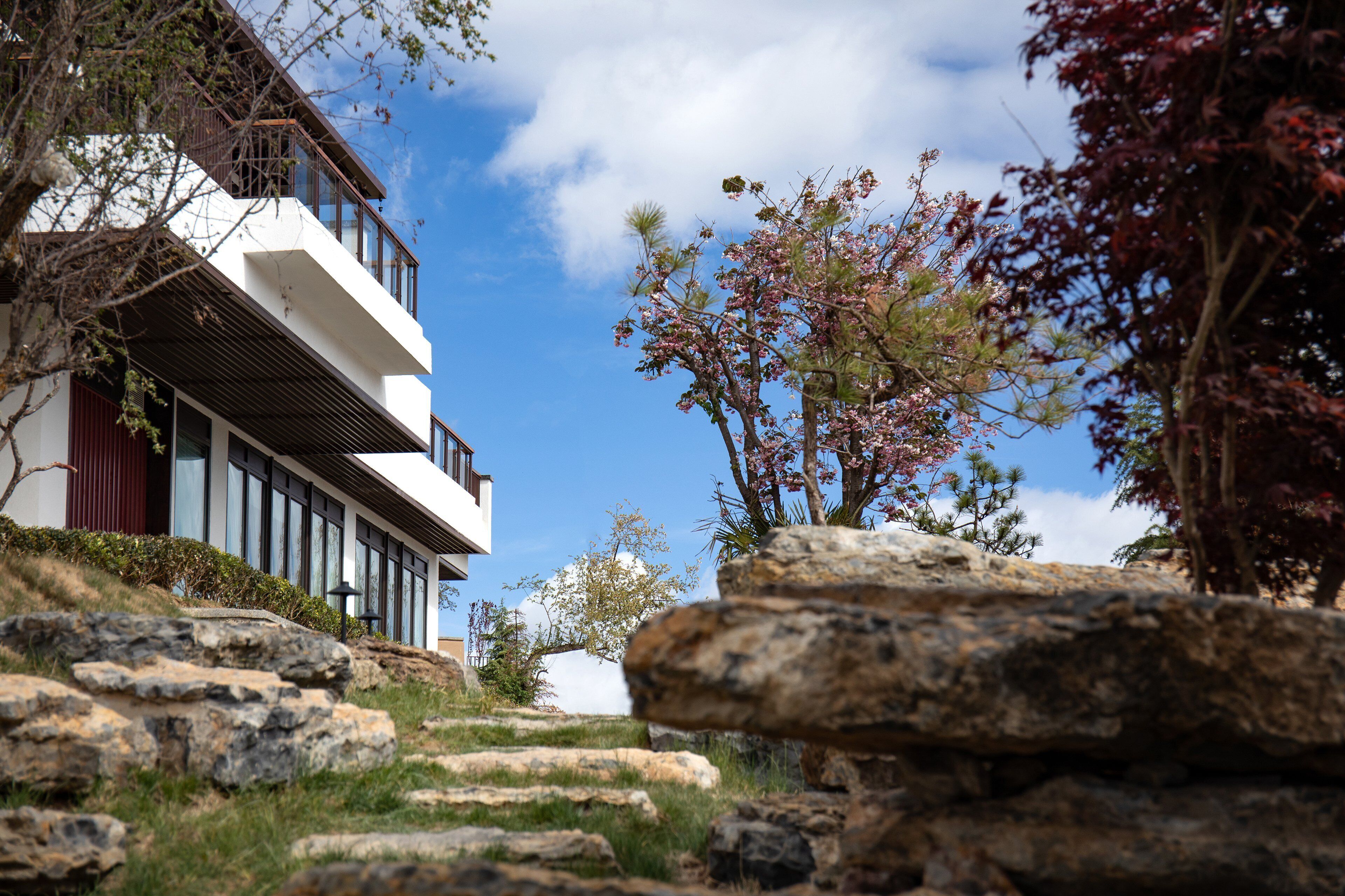 A modern building with a balcony, surrounded by rocks and trees.