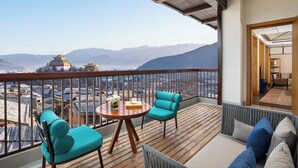 A balcony with wooden flooring, a round table with chairs, and a view of distant mountains and traditional architecture.