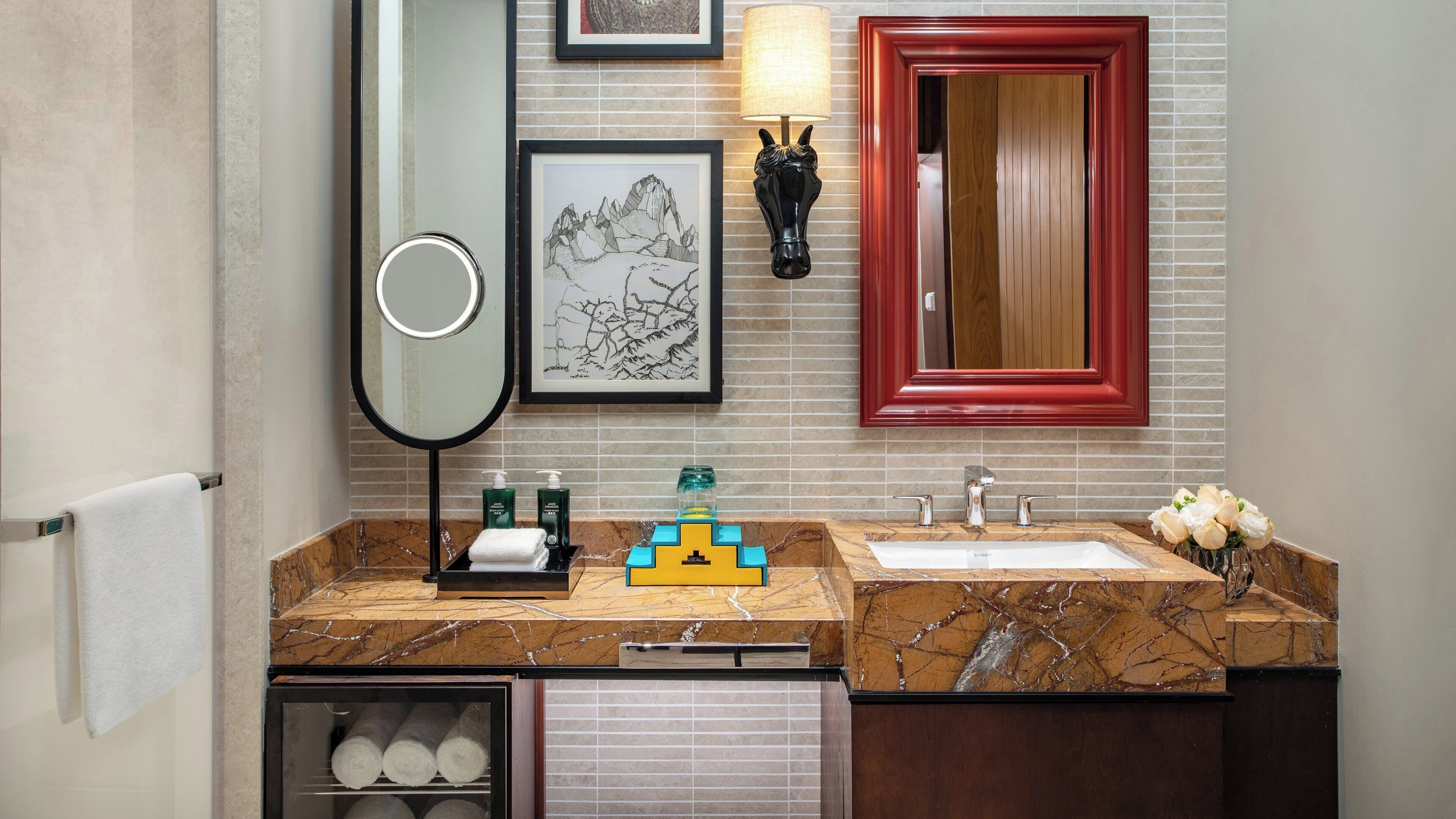 A bathroom with two sinks, a mirror, a towel rack, a small refrigerator, and a wall-mounted lamp.