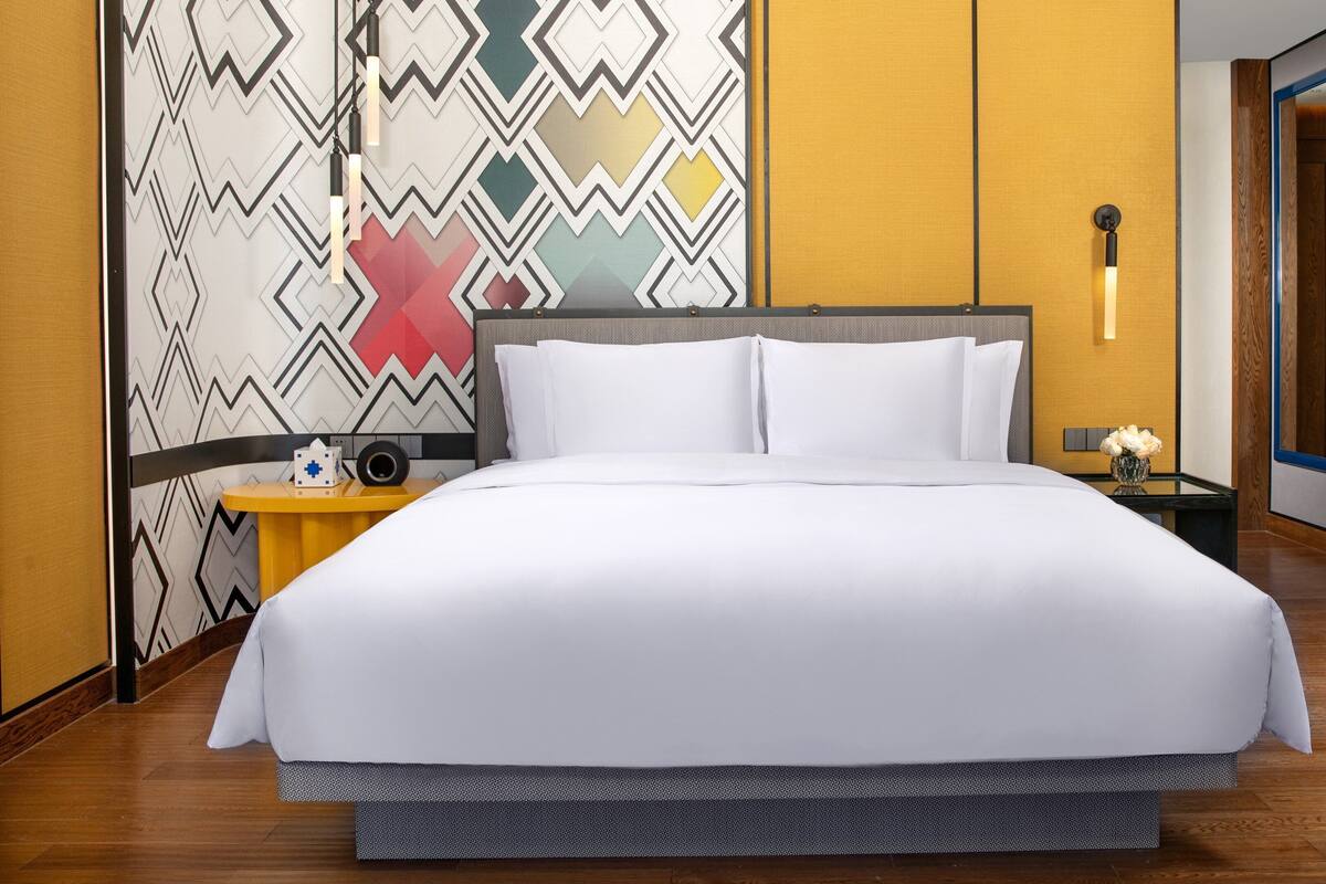 Une chambre d’hôtel avec un grand lit, une table de chevet avec une lampe et un panneau décoratif au mur.