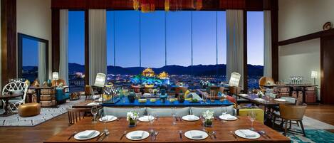 A dining area with a large table set for six, a bar area, and a view of a cityscape at dusk.