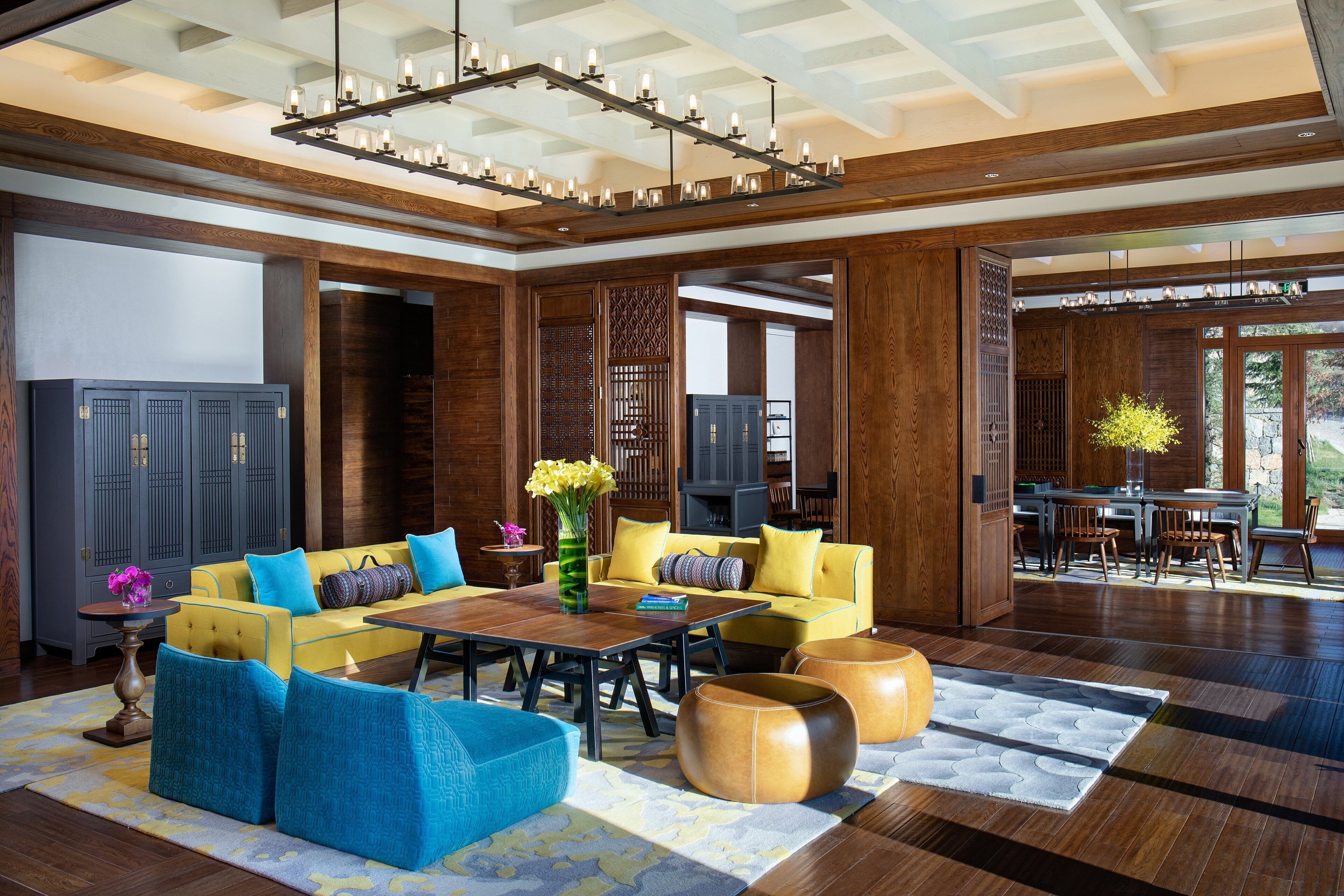 Amplia sala de estar con un sofá amarillo, cojines azules decorativos, una mesa de centro de madera y una lámpara de araña.