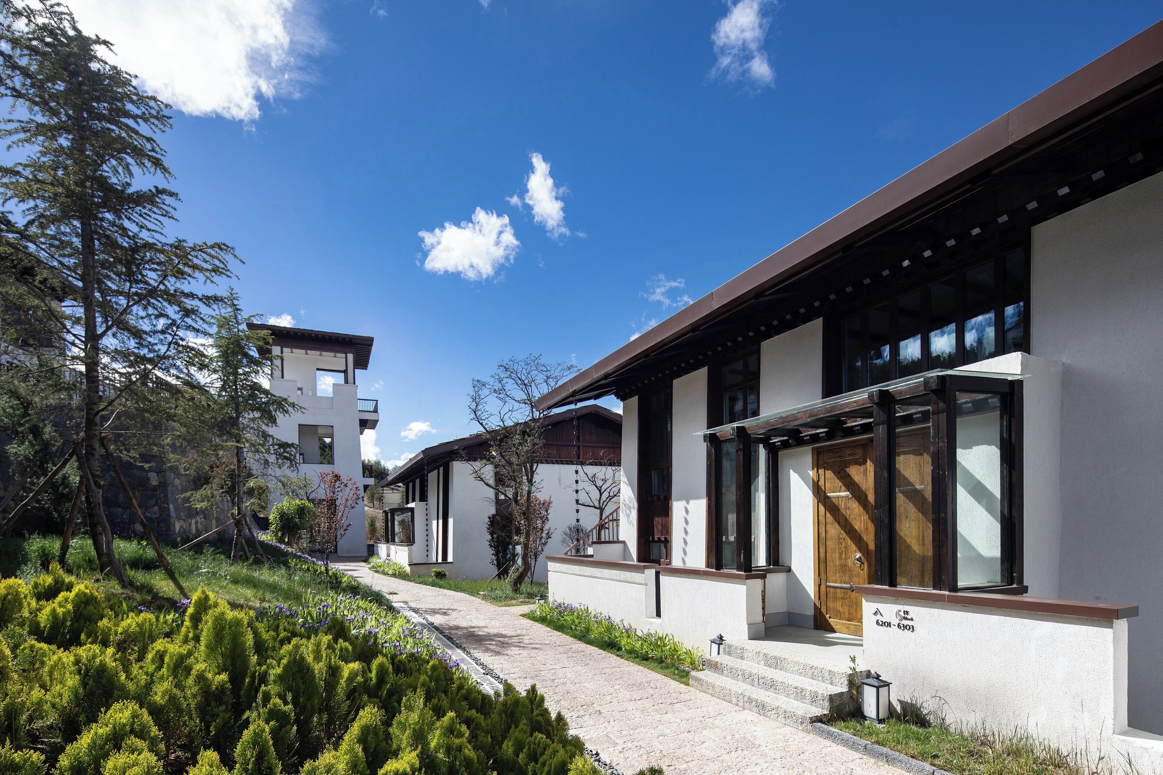Un edificio residenziale moderno con un vialetto che conduce all'ingresso, circondato dal verde e sotto un cielo sereno.