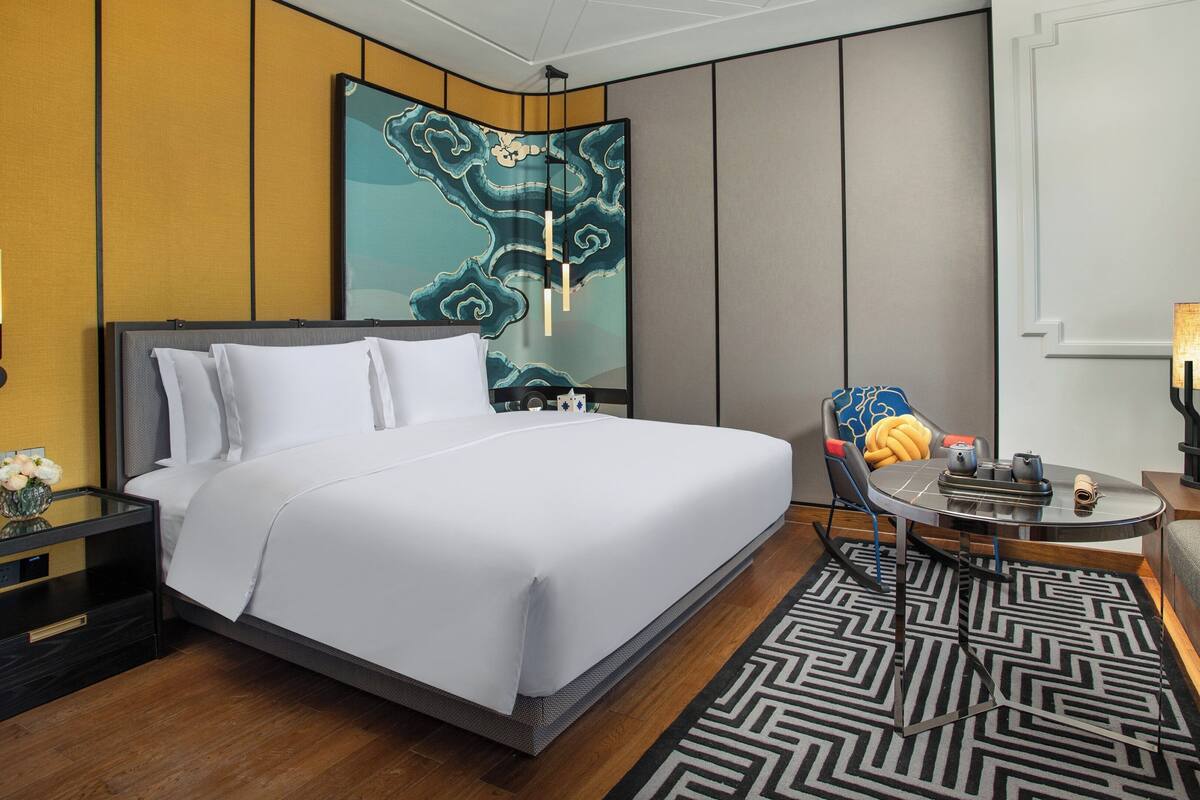 Une chambre d’hôtel avec un grand lit, un coin salon avec une table, un élément décoratif mural et une lampe.