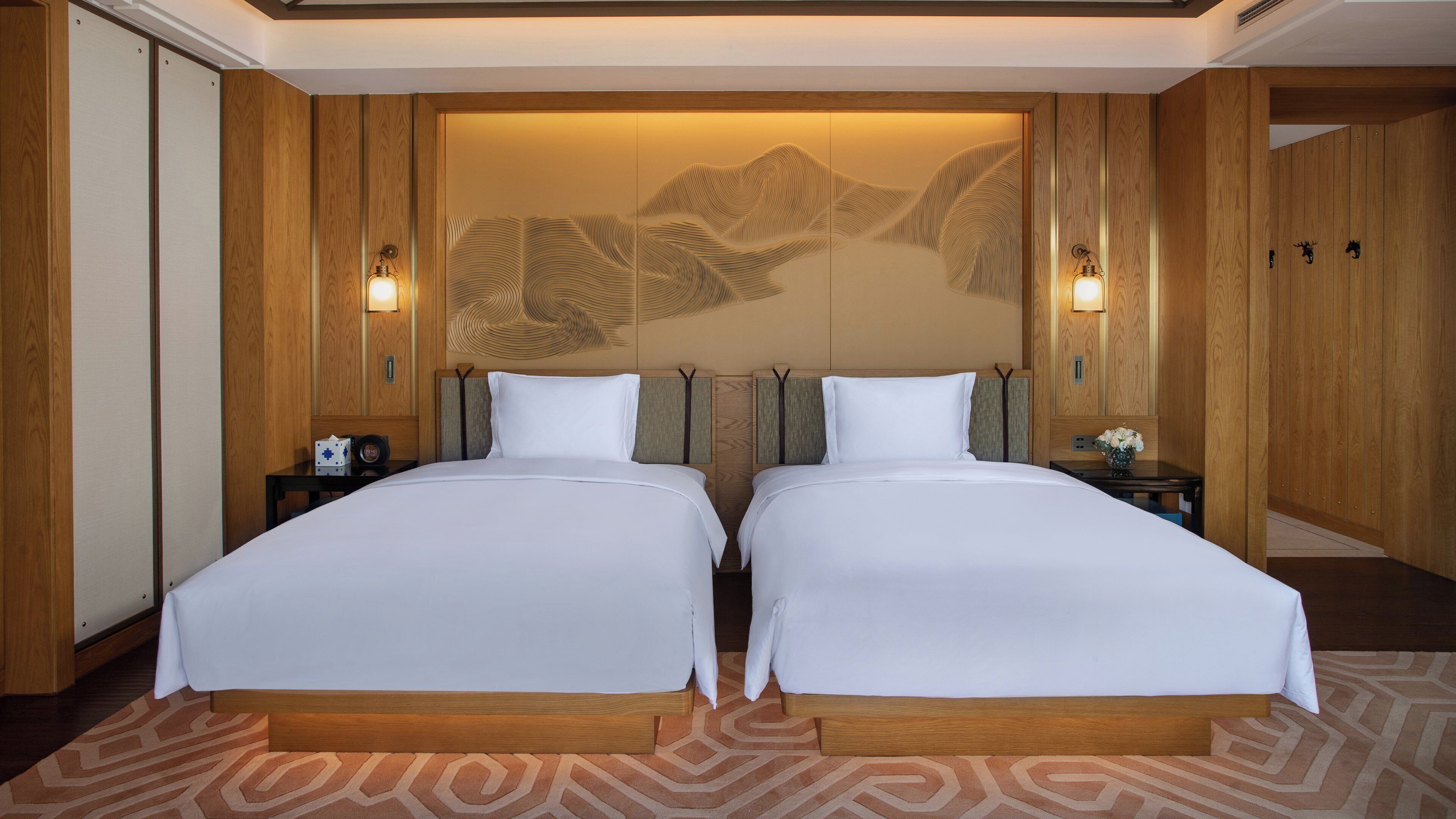 A hotel room with two beds, wooden paneling, a decorative wall, and bedside lamps.