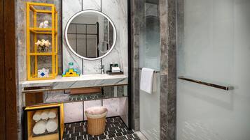 A modern bathroom with a marble vanity, a round mirror, a glass shower enclosure, and a wicker basket with towels.