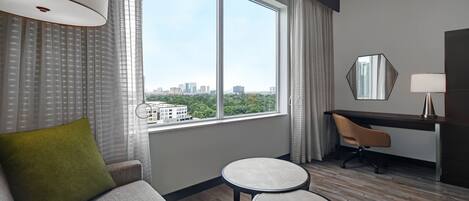 Una habitación de hotel moderna con un ventanal grande, un sofá, un escritorio y una silla.