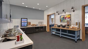 A modern kitchen with a buffet setup, a herringbone tile backsplash, and a large painting on the wall.