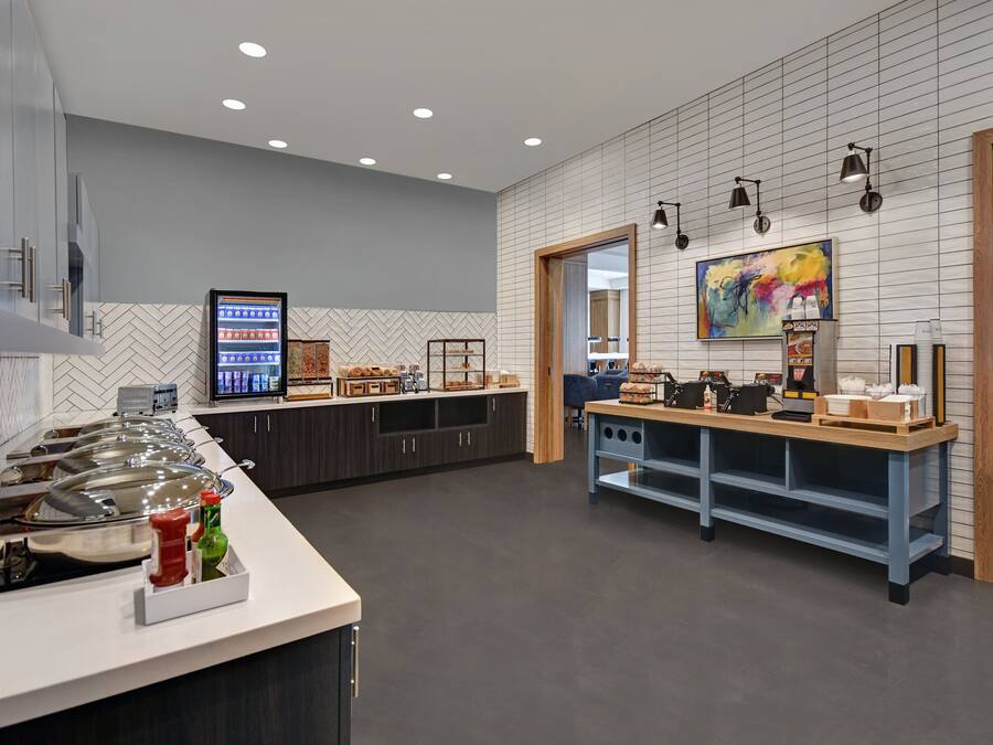 A modern kitchen with a buffet setup, a herringbone tile backsplash, and a large painting on the wall.