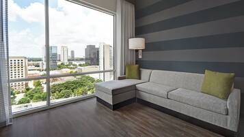 Ein modernes Wohnzimmer mit einem großen Fenster, einem grauen Sofa, einem grünen Kissen und einer Wandlampe.