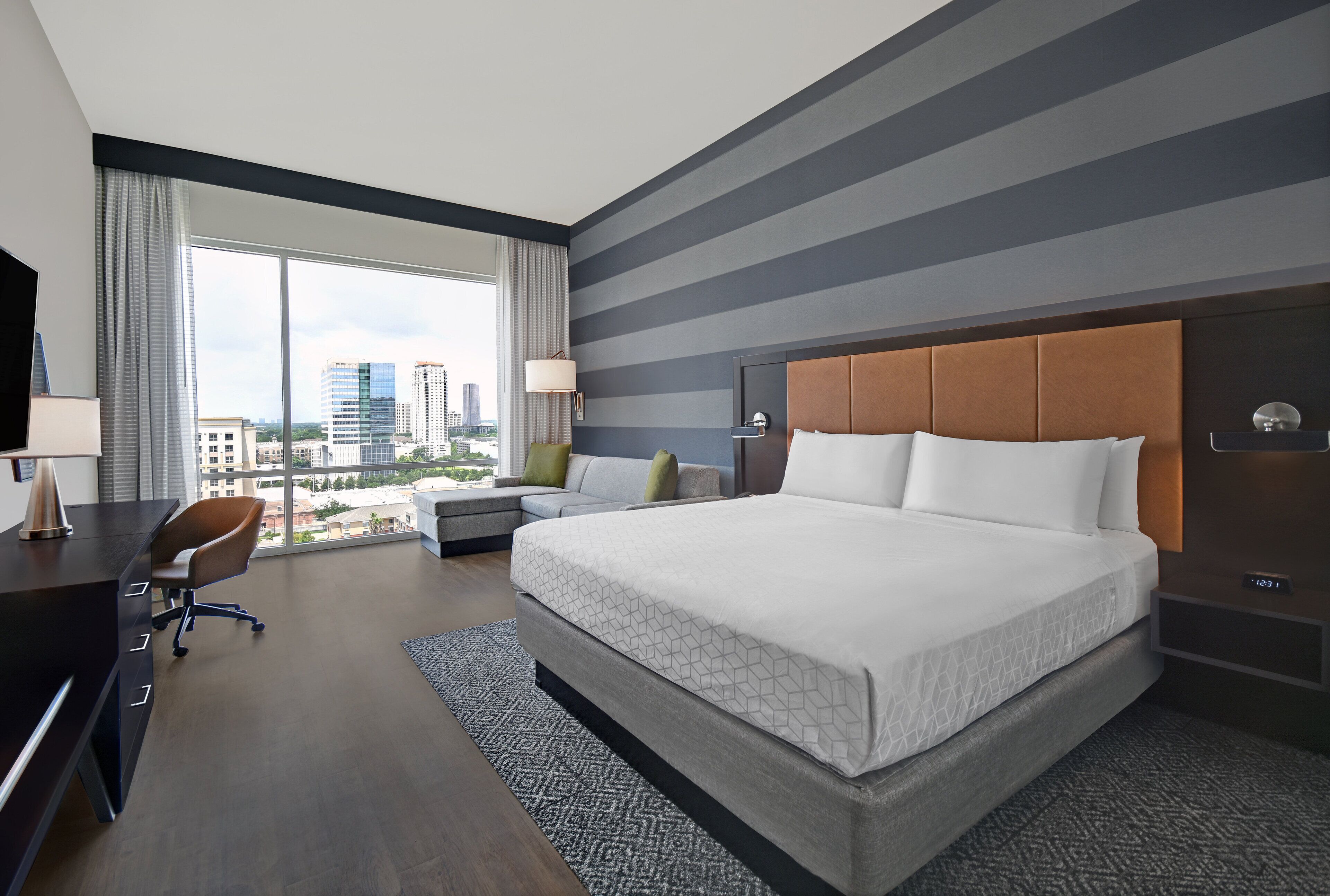 A hotel room with a large bed, a desk, a chair, and a view of the cityscape.