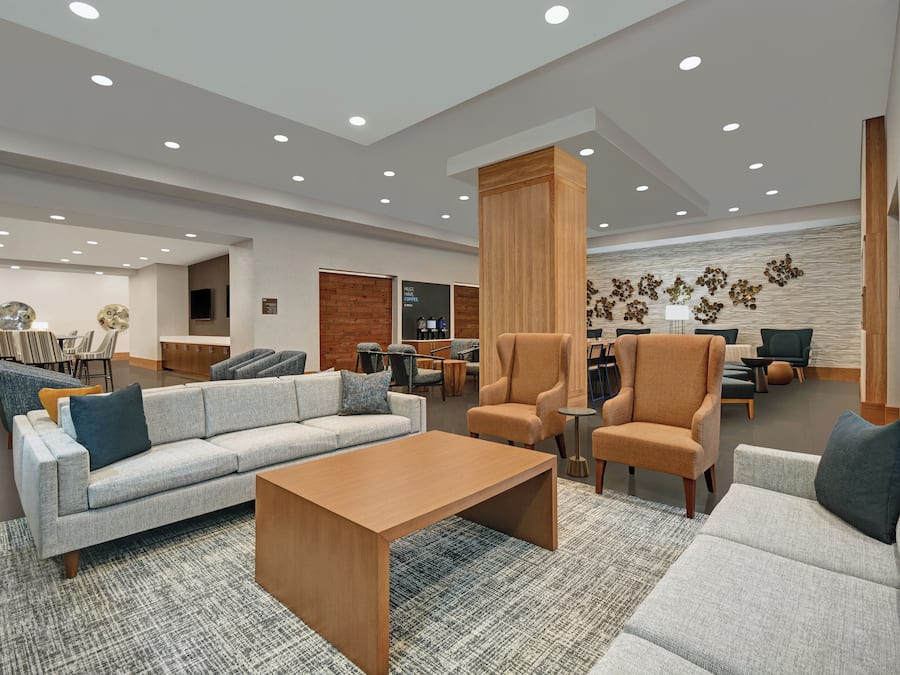 A modern lobby with a grey sofa, armchairs, a wooden coffee table, and a patterned rug.