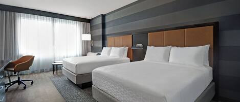 A hotel room with two beds, a desk, and a chair.