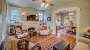 A spacious living room with a fireplace, wicker furniture, and a ceiling fan. - New Braunfels Bungalow~Near Downtown (New Braunfels)