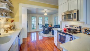 A kitchen with white cabinets, a stainless steel microwave, and a round dining table with chairs. - New Braunfels Bungalow~Near Downtown (New Braunfels)