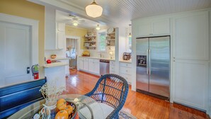 A spacious kitchen with white cabinetry, a stainless steel refrigerator, and a dining area with a wicker chair and a table set with pumpkins. - New Braunfels Bungalow~Near Downtown (New Braunfels)