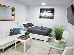 Quarto moderno com cama branca, sofá branco, mesa de centro de vidro e um espelho grande.