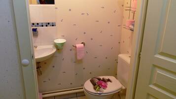 A bathroom with a toilet, sink, and a small shelf with toiletries.