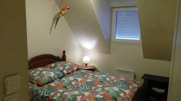 A bedroom with a bed, a nightstand, a lamp, a window with blinds, and a wall-mounted bird.