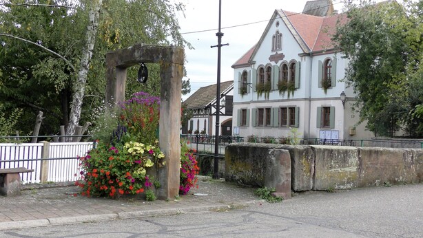 En traditionel bygning med en hvid facade og grønne skodder, en stenvæg med blomster og en belagt gade.