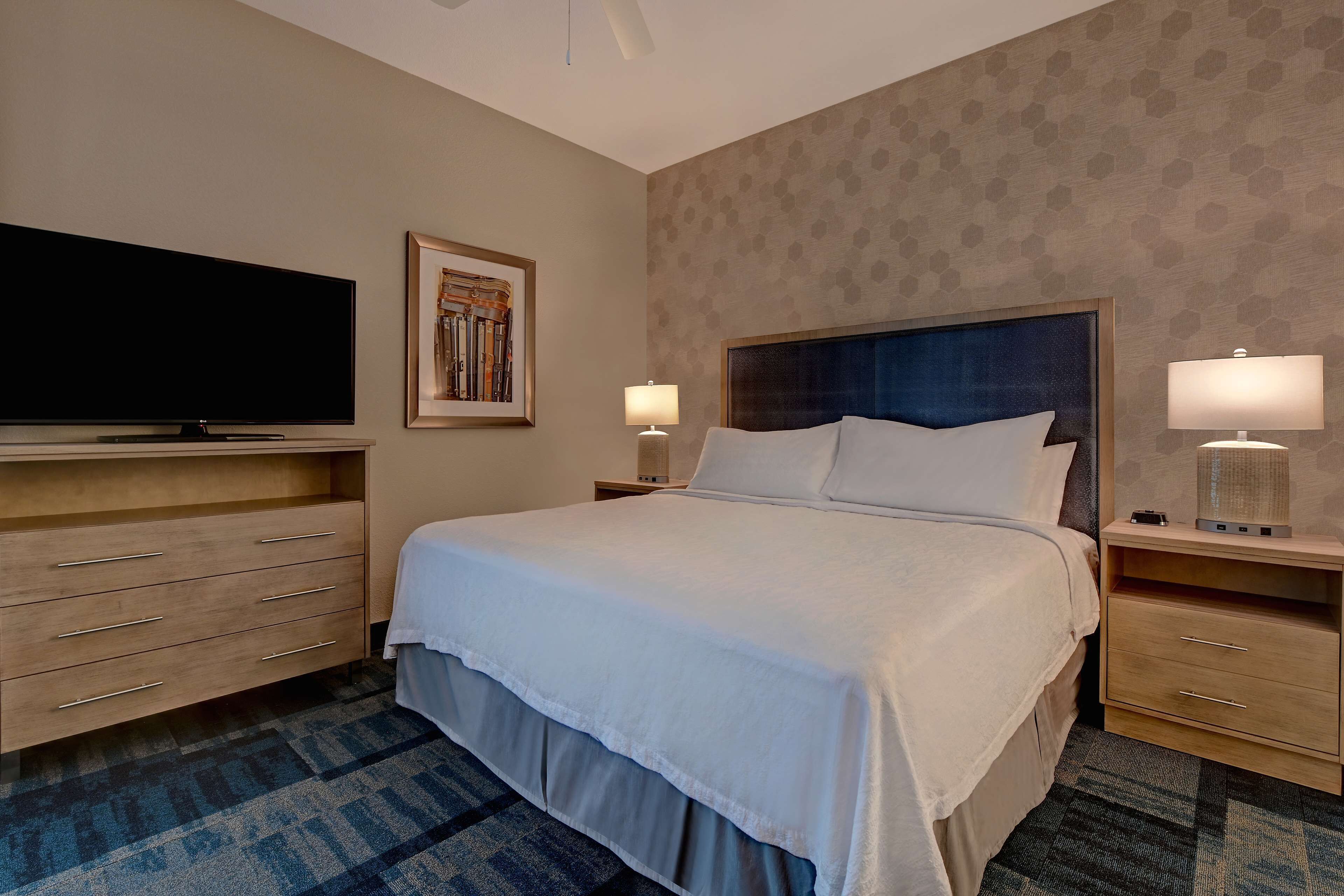 Camera d'albergo con un letto grande, una TV a schermo piatto, una scrivania con una lampada e un tappeto decorato.