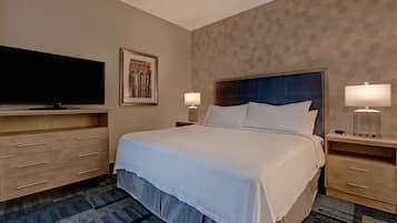 A hotel room with a large bed, a flat-screen TV, a desk with a lamp, and a patterned carpet.