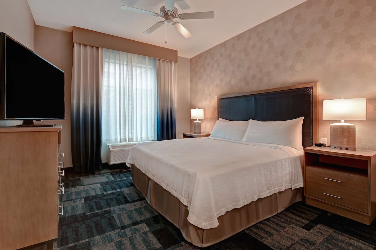 Una habitación de hotel con una cama grande, un televisor de pantalla plana, un escritorio y un ventilador de techo.