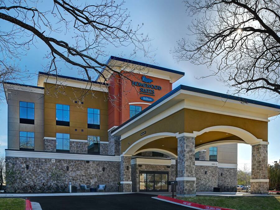 Un hotel moderno con fachada de piedra, un cartel llamativo de Homewood Suites y una zona de entrada cubierta.