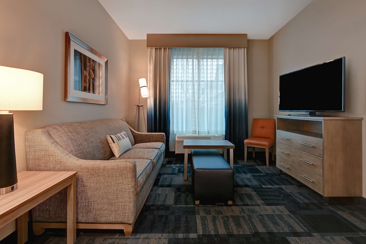 Habitación de hotel con sofá, una mesita, televisor, escritorio y silla.