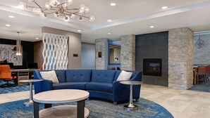 Un vestíbulo moderno con un sofá seccional azul, dos mesas redondas, un muro decorativo y una chimenea de piedra.