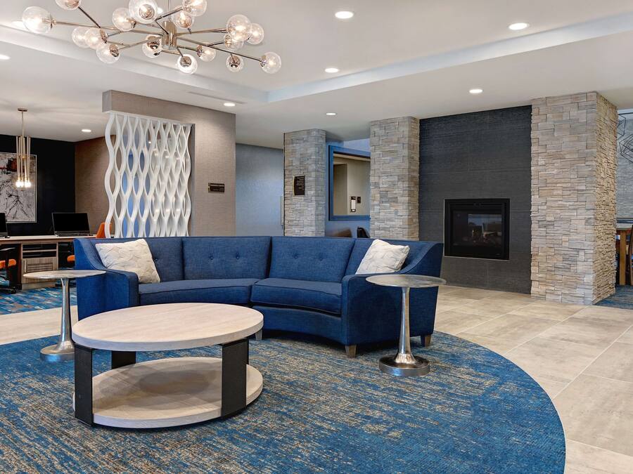 A modern lobby with a blue sectional sofa, two round tables, a decorative wall, and a stone fireplace.