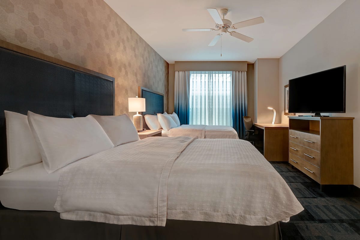 Habitación de hotel con dos camas, televisión, escritorio y ventilador de techo.