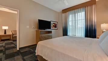 A hotel room with a large bed, a flat-screen TV, a desk with a lamp, and a window with curtains.