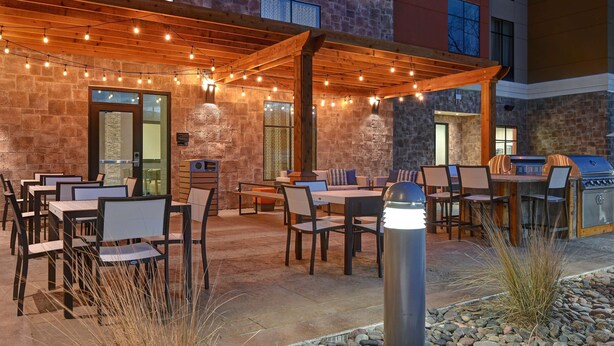 Un patio al aire libre con mesas y sillas, una parrilla y luces colgantes.