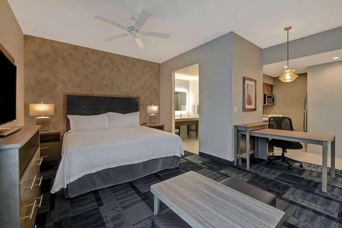 Habitación de hotel con cama, escritorio, silla y ventilador de techo.