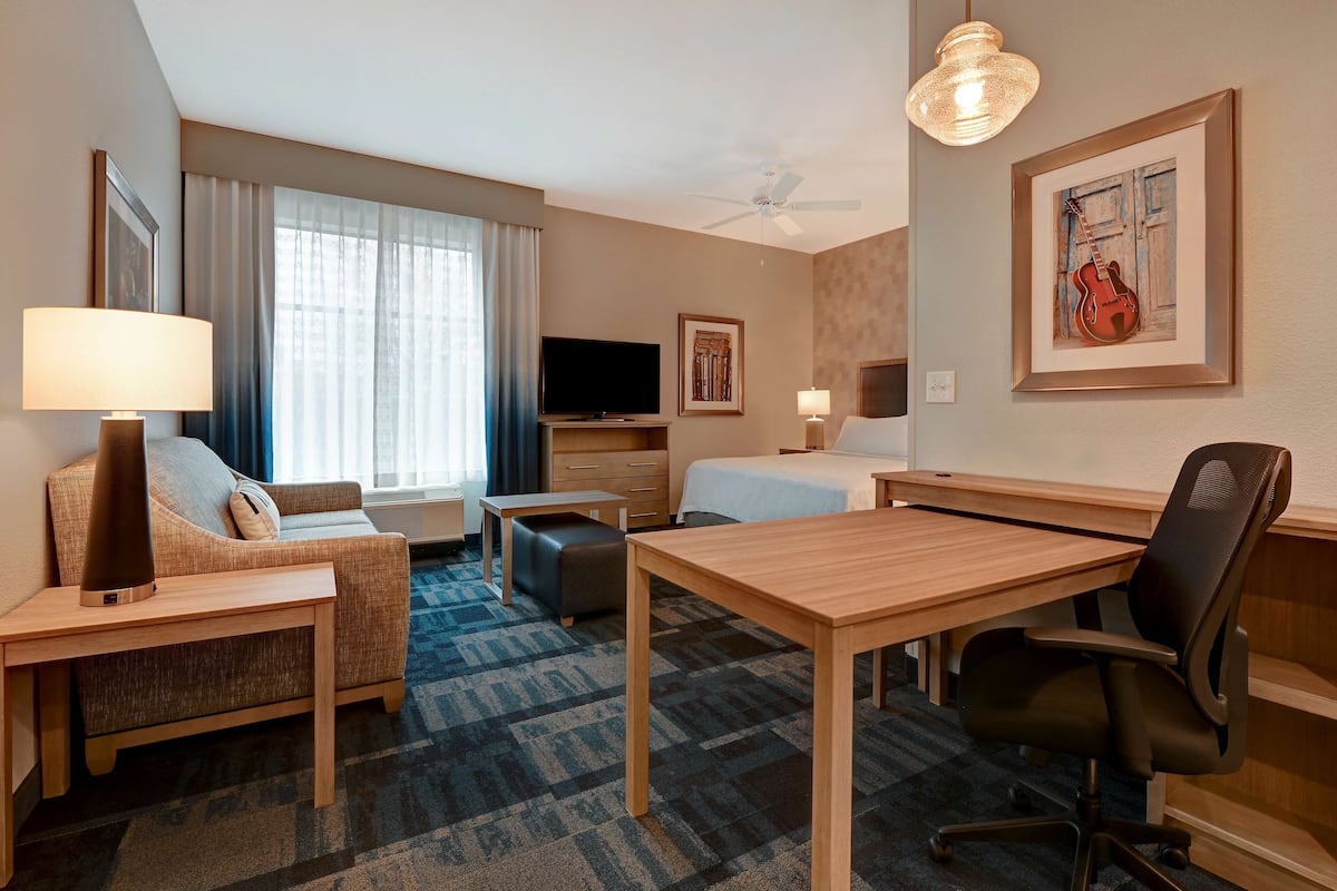 Habitación de hotel con sofá, escritorio, silla, cama, televisión y ventilador de techo.