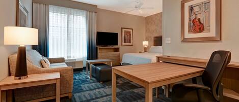 A hotel room with a sofa, a desk, a chair, a bed, a TV, and a ceiling fan.