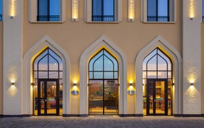 L’entrée d’un hôtel, ornée de trois fenêtres en arc, chacune portant une enseigne indiquant « Hampton ».