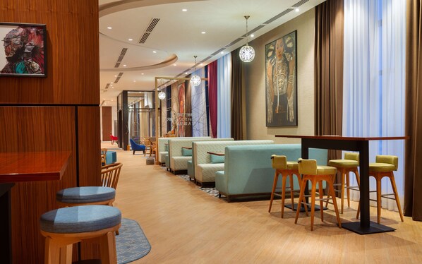 Un hall d’hôtel moderne avec un bar, des espaces aménagés pour s’asseoir et des œuvres d’art accrochées aux murs.