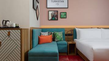 Habitación de hotel con un sofá color turquesa, una cama y una pared con cuadros, incluyendo uno con la etiqueta 'TURKISTAN'.