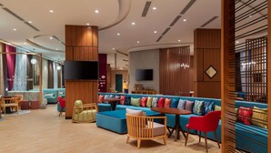 Un salon moderne avec un canapé bleu, des chaises en bois et un téléviseur fixé au mur.