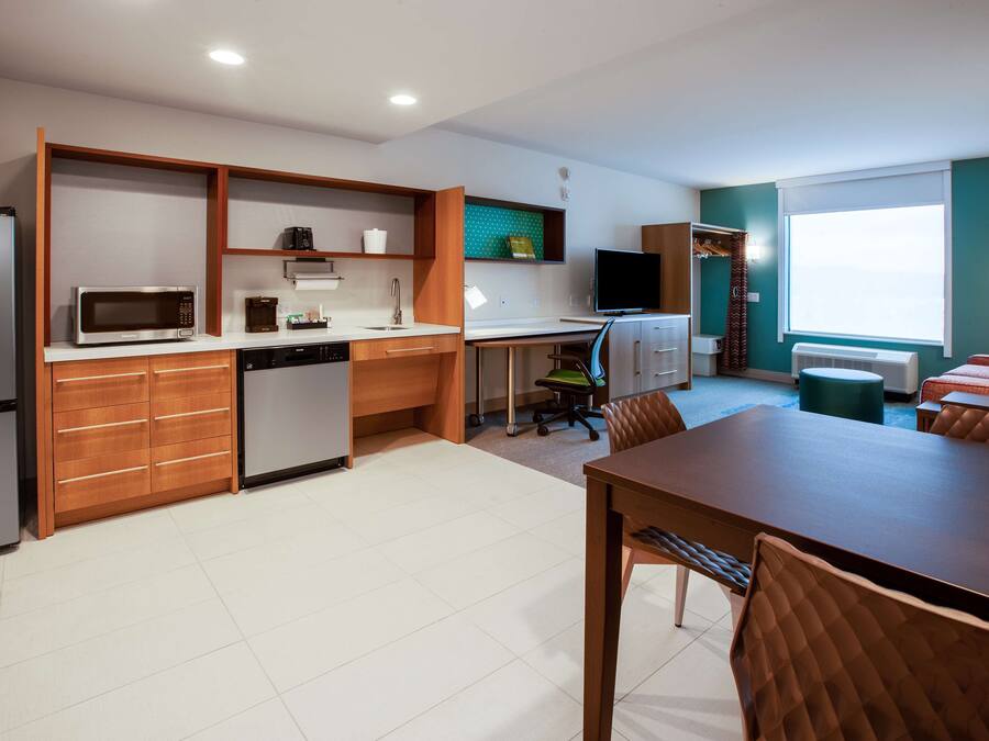 Cocina compacta con electrodomésticos modernos, comedor con mesa y sillas de madera, y vista al exterior a través de un ventanal grande.